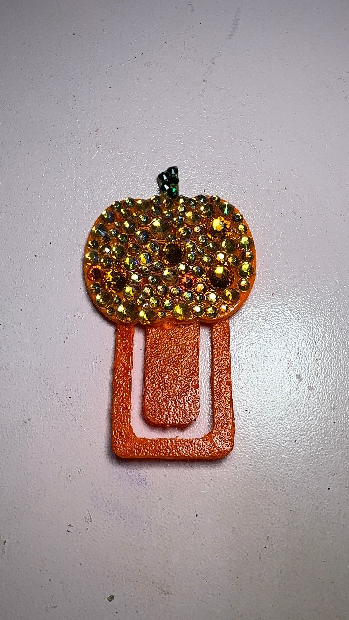 The TipClip by Viva La Bombshell Burlesque, a pumpkin-shaped paperclip with orange and yellow rhinestones and a green glittery stem.