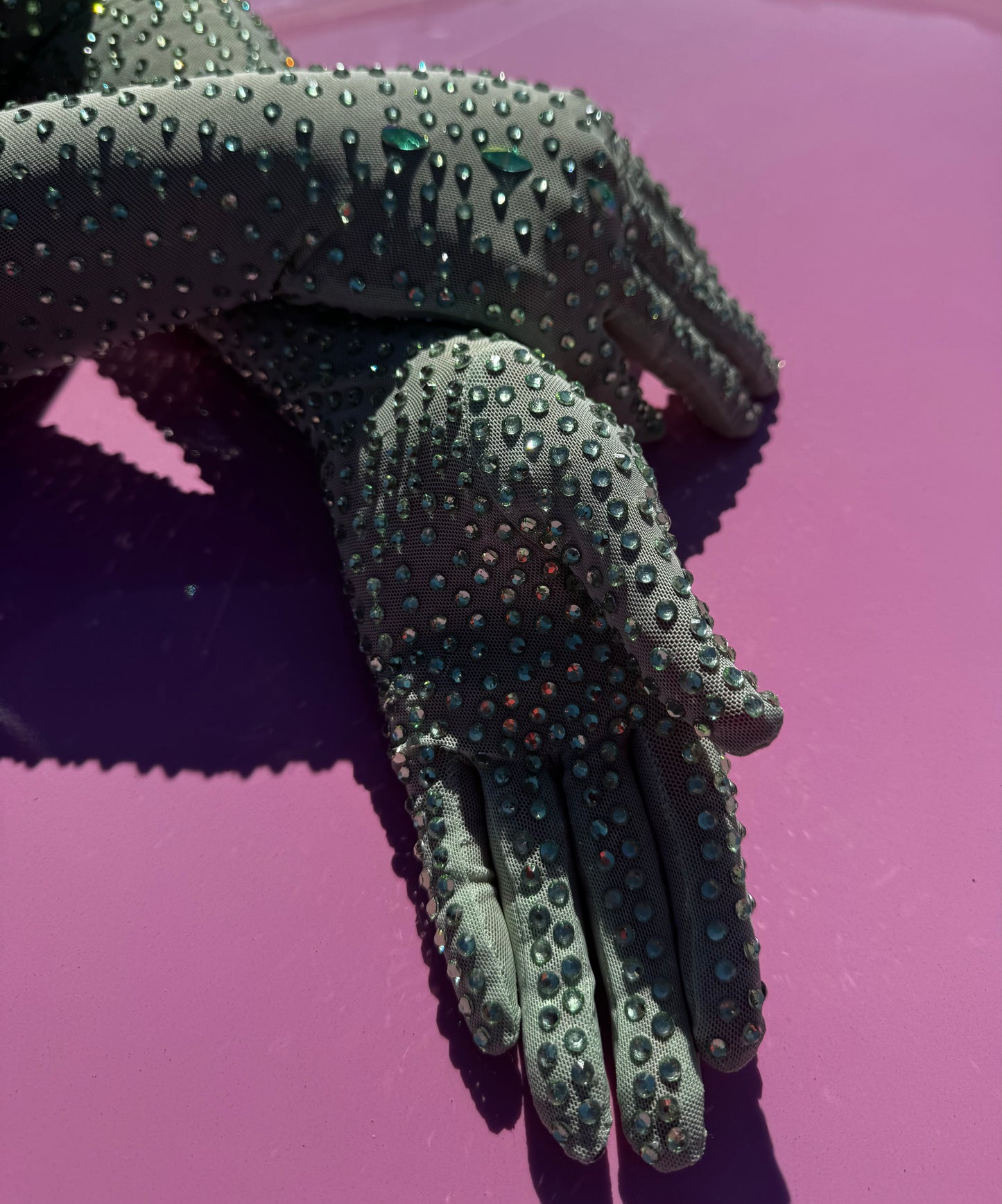 A close-up of two hands wearing Viva La Bombshell Burlesque’s The Mint Special - Rhinestone Gloves, sparkling with shiny rhinestones and resting on a bright pink surface.
