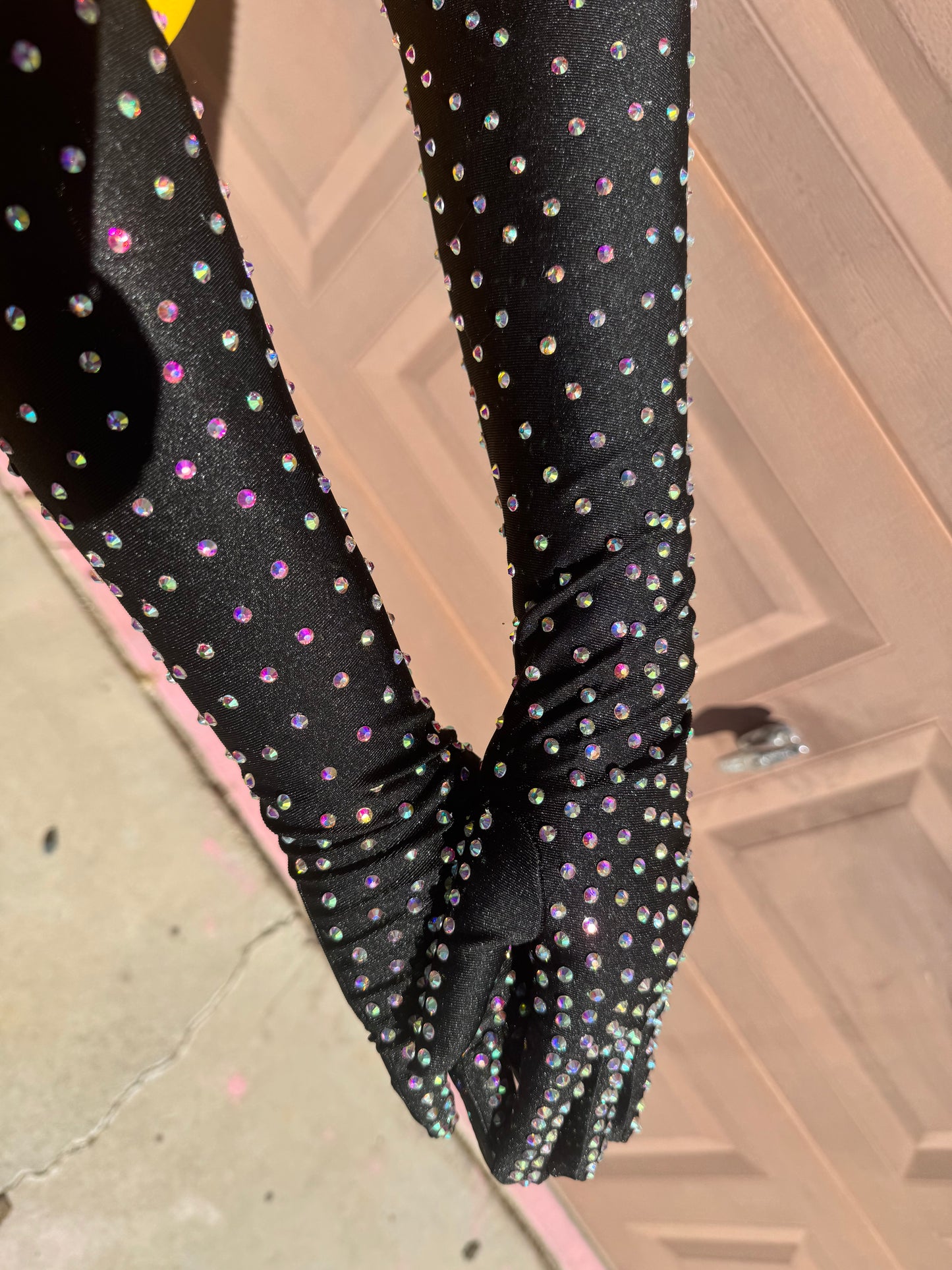 A person wearing Viva La Bombshell Burlesque's Classic Rhinestone Gloves stands outside by a beige garage door, sunlight catching the sparkling rhinestones on these glamorous accessories.