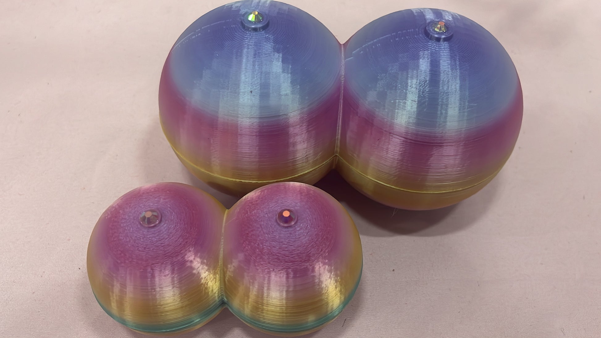 Four round, dome-shaped Boobie Boxes by Viva La Bombshell Burlesque in gradient hues—blue, purple, pink, yellow, and teal—feature gem-like beads on top. Stylish 3D-printed storage for pasties, shown in pairs on a light background.