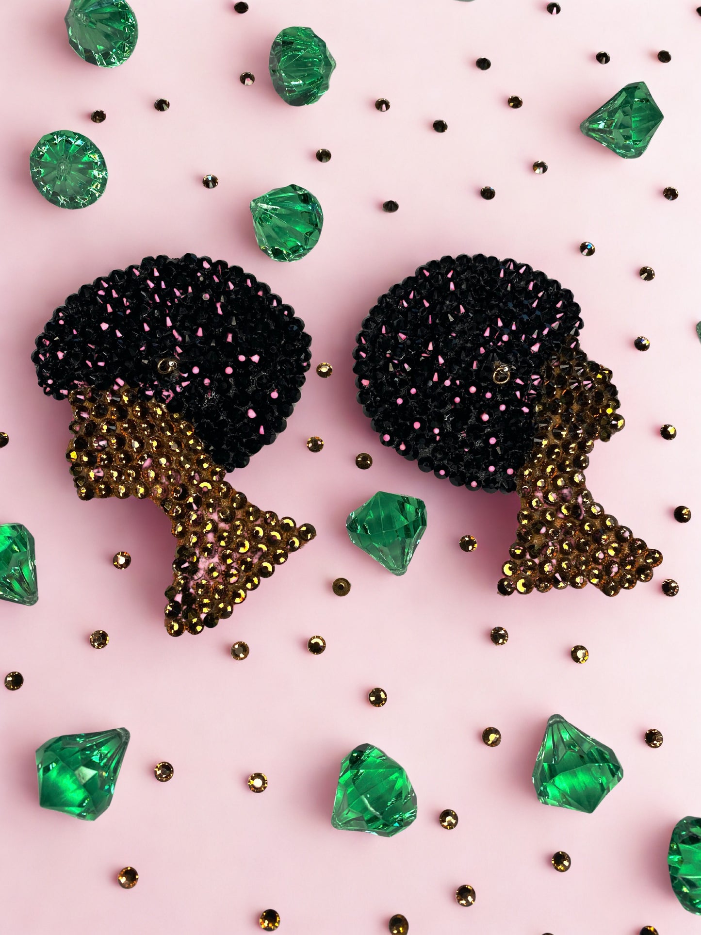 Beaded earrings shaped like a woman’s profile with an afro, inspired by Viva La Bombshell Burlesque's Afro Girl Pasties, are displayed on a pink surface with green gem-like stones and gold beads.