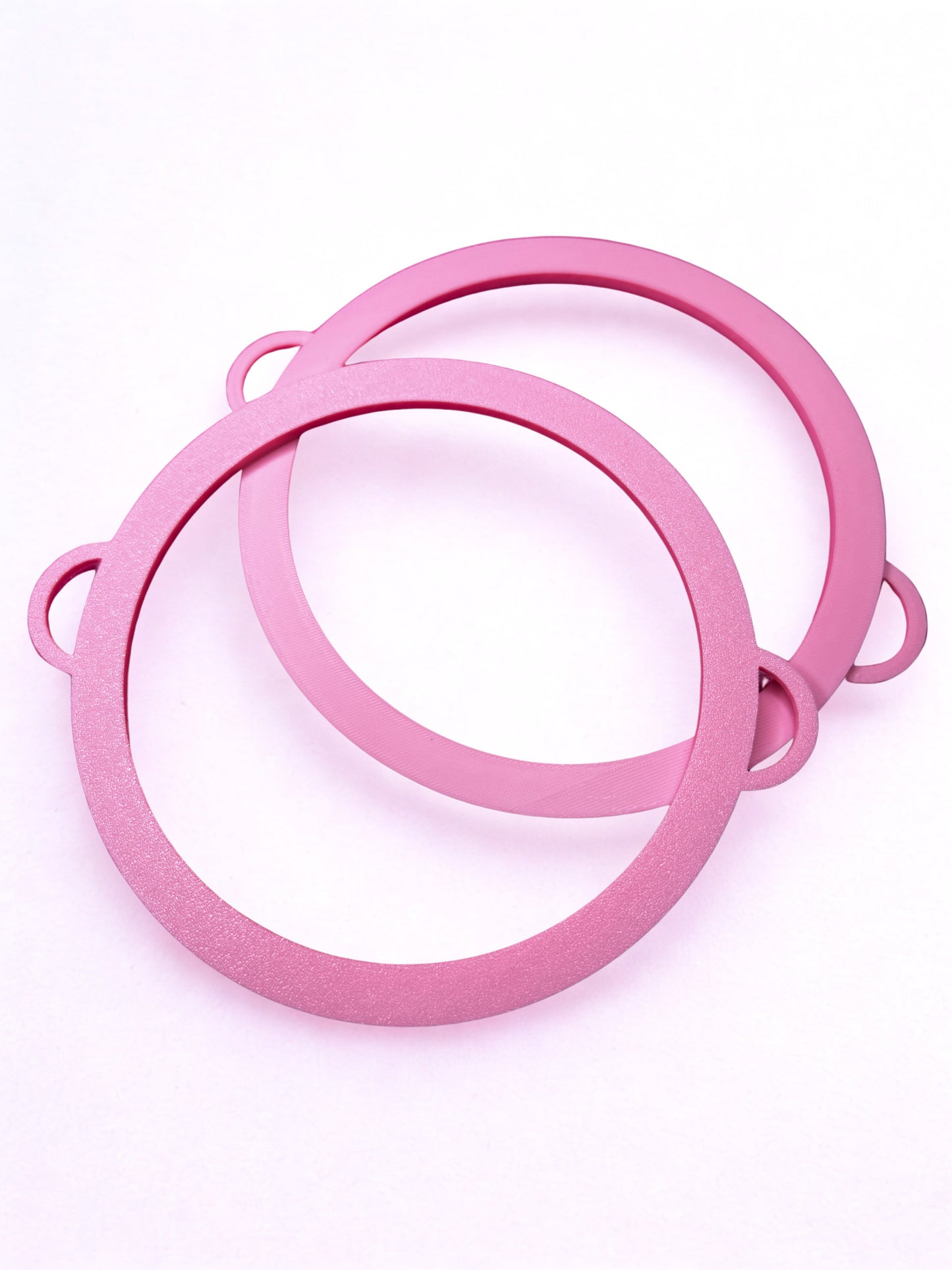 Two overlapping pink Circle Bangle - Boa Attachments by Viva La Bombshell Burlesque, made of plastic with small raised tabs, resembling 3D printed bangles, displayed on a white background.