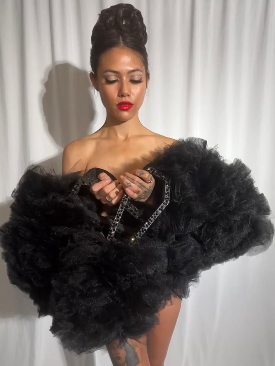 Woman holding a large black tulle boa with 3D printed coffin shaped bangles  against a white curtain background