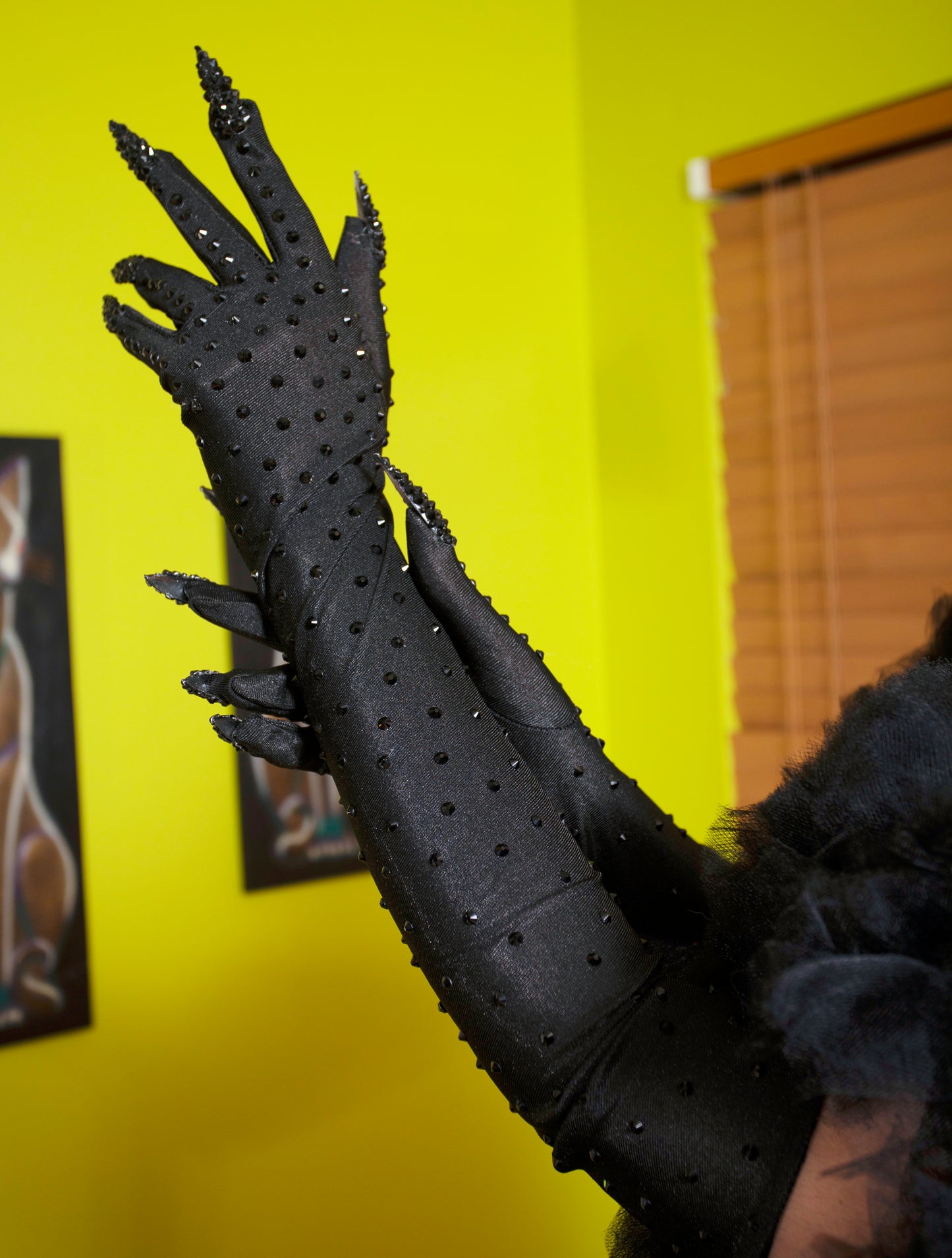 Black gloves with clawed tips held up against a yellow wall.