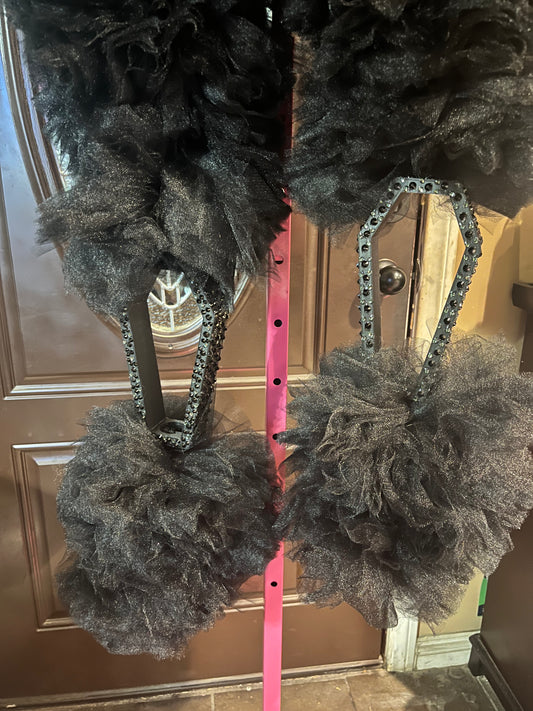 Close-up of two black tulle pom-poms attached to black rhinestone coffin bangles, hanging from a bright pink vertical pole, with a brown door in the background.