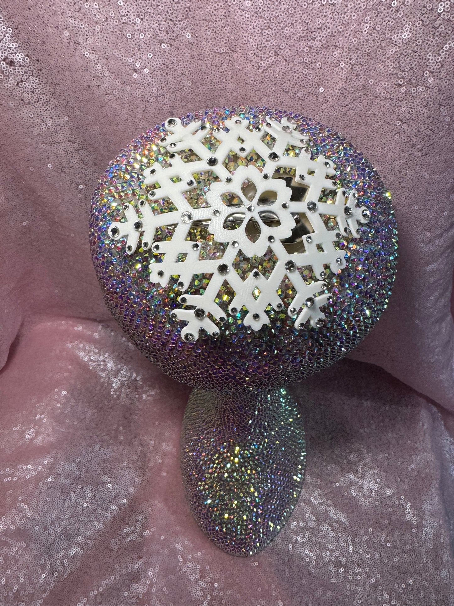 The Snow Queen Fascinator by Viva La Bombshell Burlesque is a sparkling, iridescent mushroom-shaped headpiece with rhinestones, floral and geometric patterns, and a decorative white snowflake, displayed on pink glittery fabric.