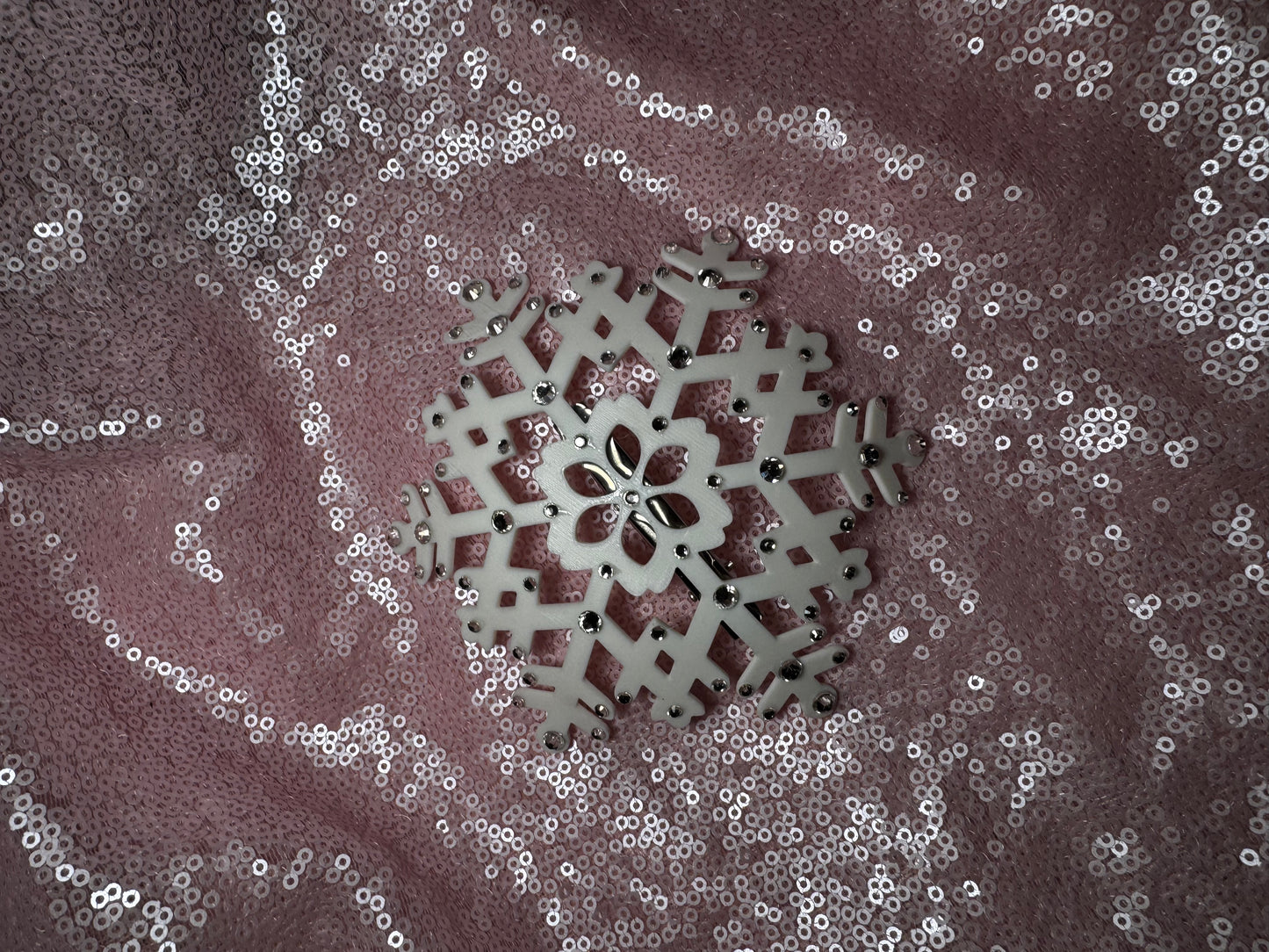 A white snowflake on pink fabric from Viva La Bombshell Burlesque's Snow Queen Fascinator, ideal for accenting a winter fascinator or rhinestone snowflake headpiece.