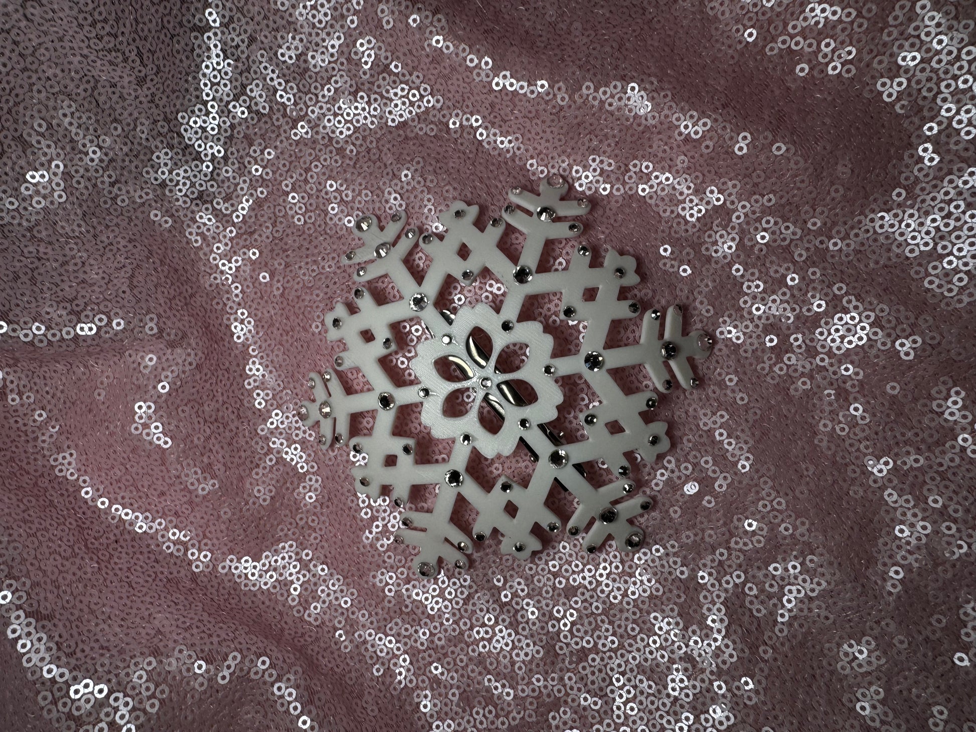 A white snowflake on pink fabric from Viva La Bombshell Burlesque's Snow Queen Fascinator, ideal for accenting a winter fascinator or rhinestone snowflake headpiece.