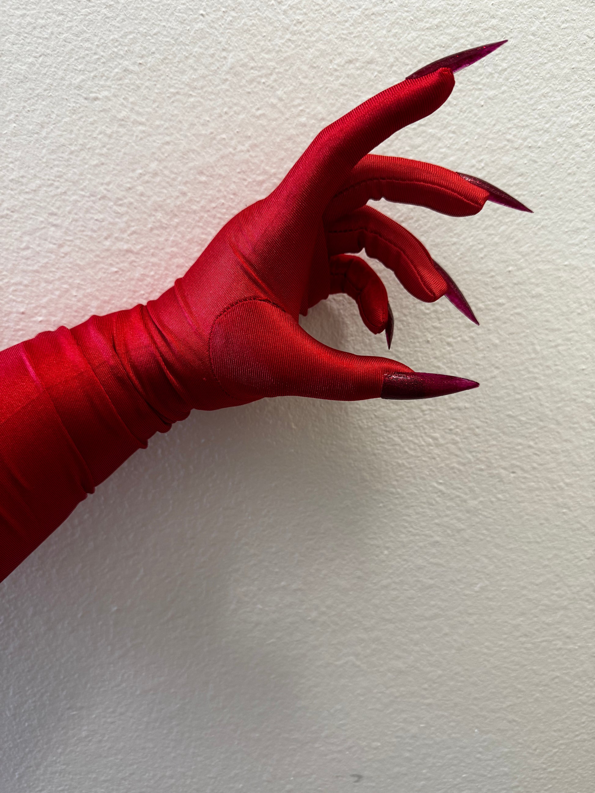 A hand models the Viva La Bombshell Burlesque DIY Kitty Claw Gloves—tight gloves with long, pointed dark red stiletto nails—posed against a light wall, fingers slightly curled for dramatic effect.