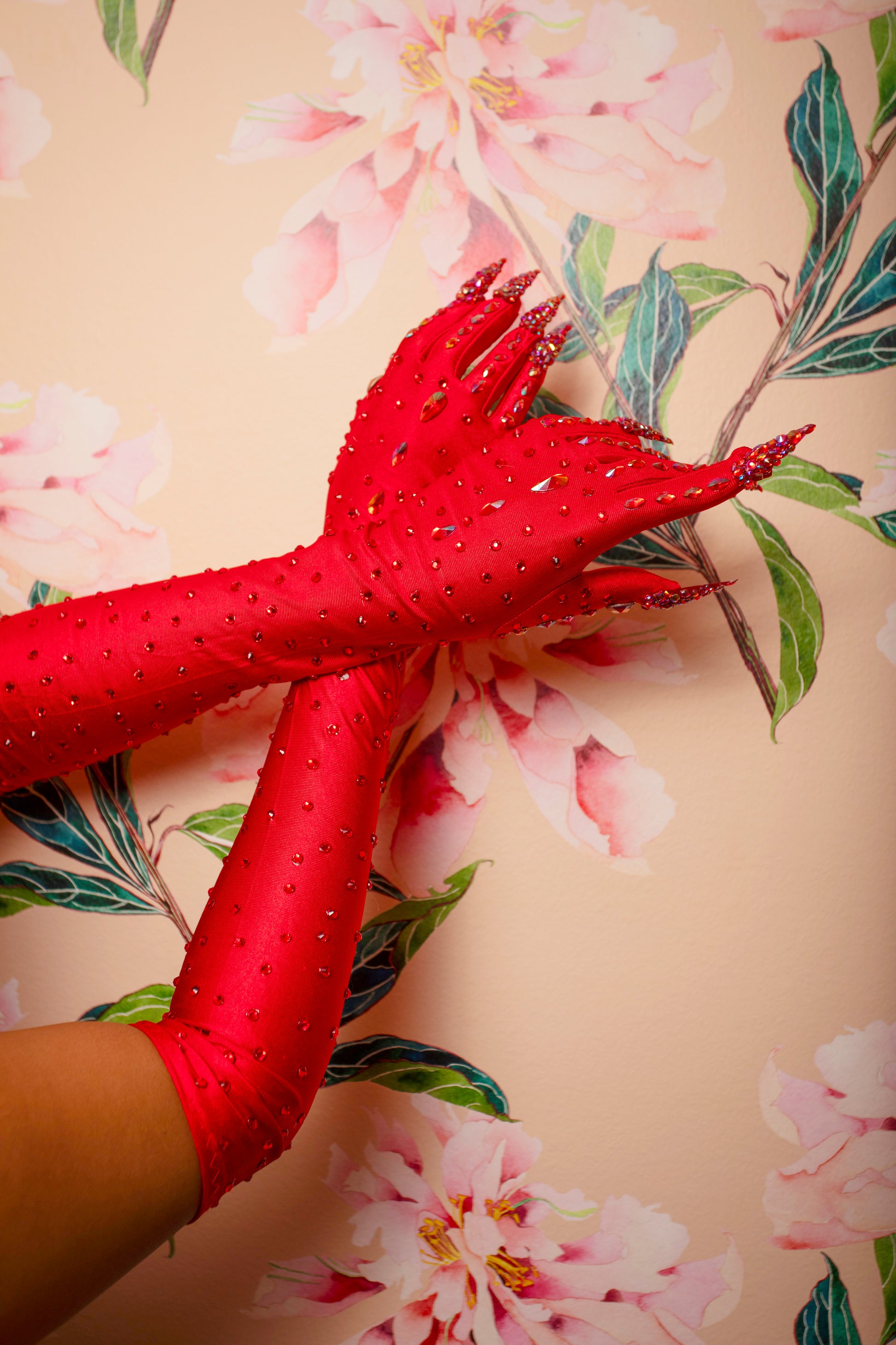 Two arms wearing Viva La Bombshell Burlesque’s Kitty Claw Gloves (AB Rhinestones) - Original are crossed at the wrists and pressed against a wall with a pink floral pattern.