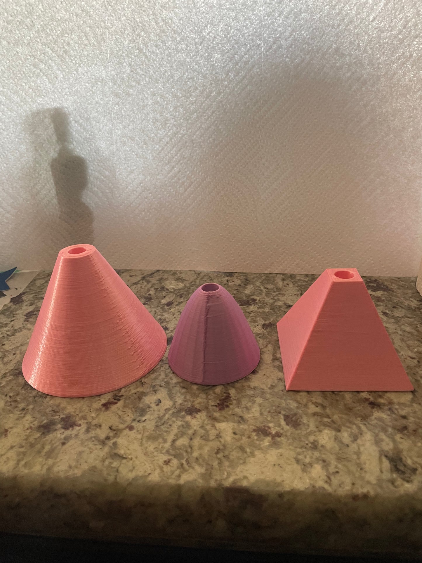 Three Boa Charms by Viva La Bombshell Burlesque—a large pink cone, a smaller purple cone, and a pink square pyramid—sit on a marbled surface. Each painted charm features a hole at the top for easy attachment.