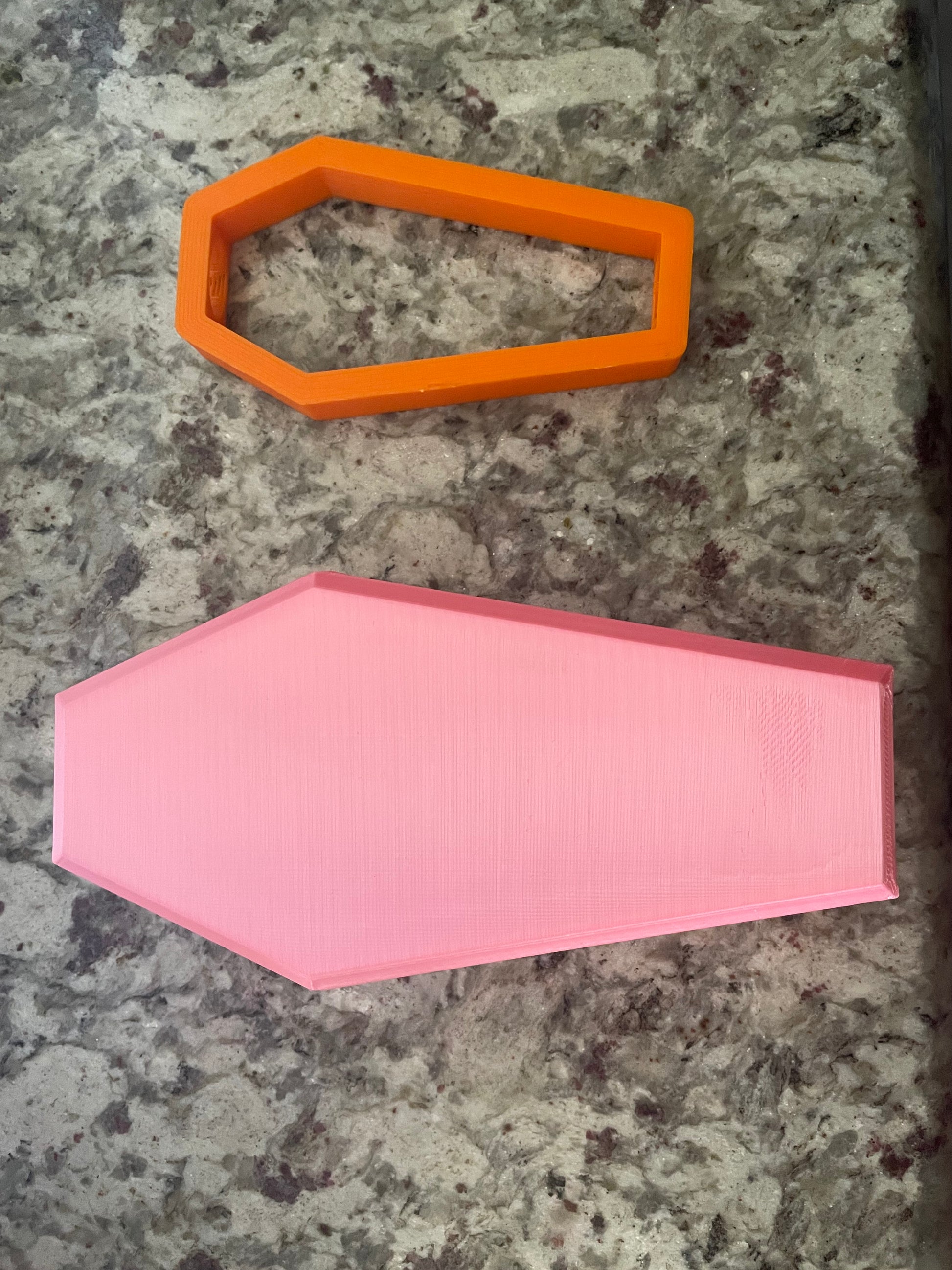 A 3D printed orange Boa Charms attachment and a larger pink base by Viva La Bombshell Burlesque are placed on a speckled countertop.