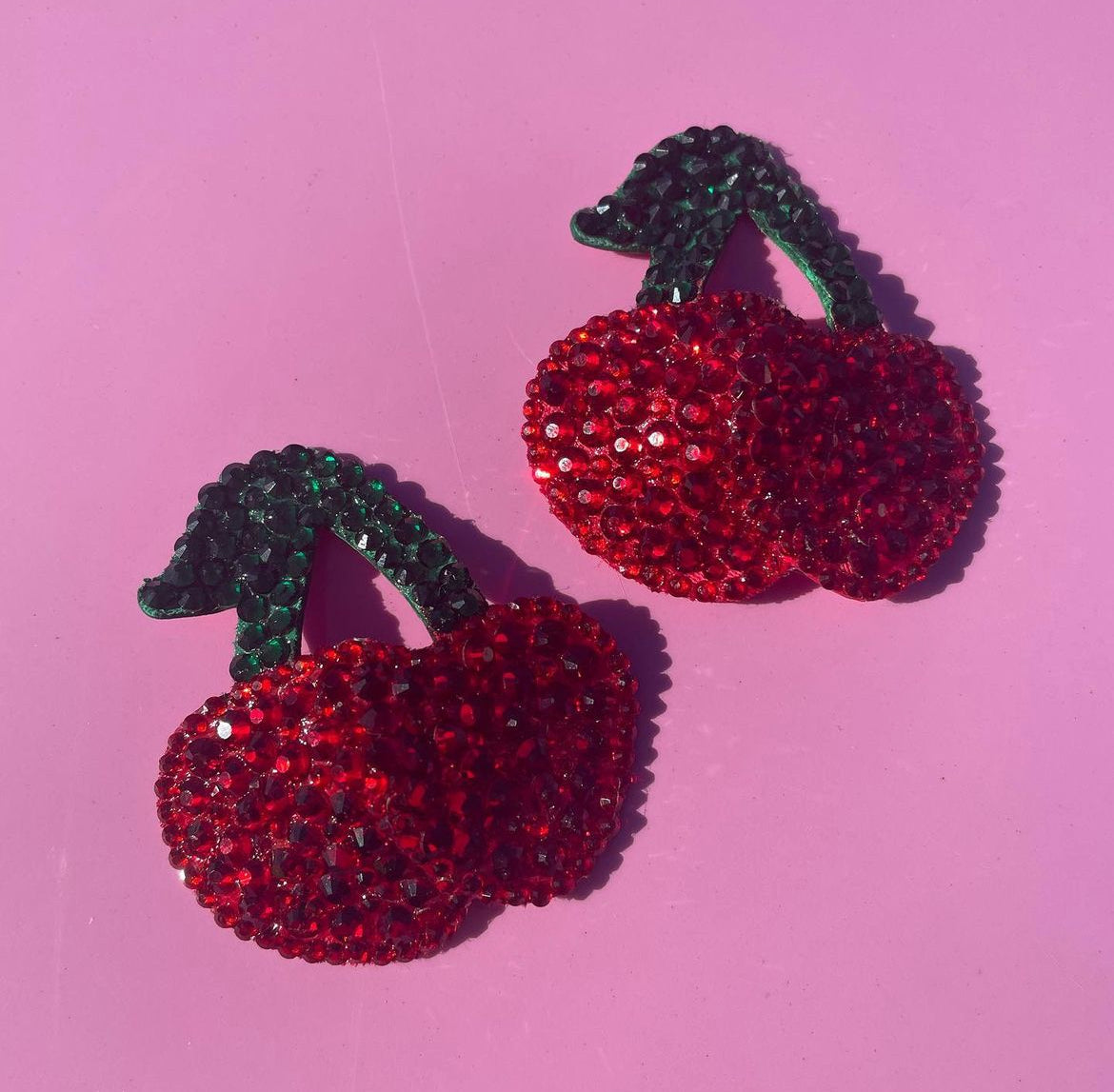 Cherry Pasties by Viva La Bombshell Burlesque feature cherry shapes with red and green crystals on a pink base and a vinyl backing for comfort.