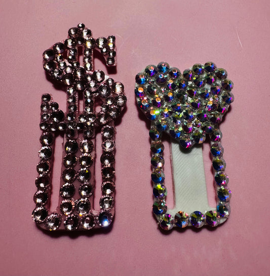 Two rhinestone hair clips from Viva La Bombshell Burlesque—one dollar sign, one beer mug—sparkle with multicolored gems on a pink surface, adding playful flair and nodding to wearable tech trends like TipSlider.