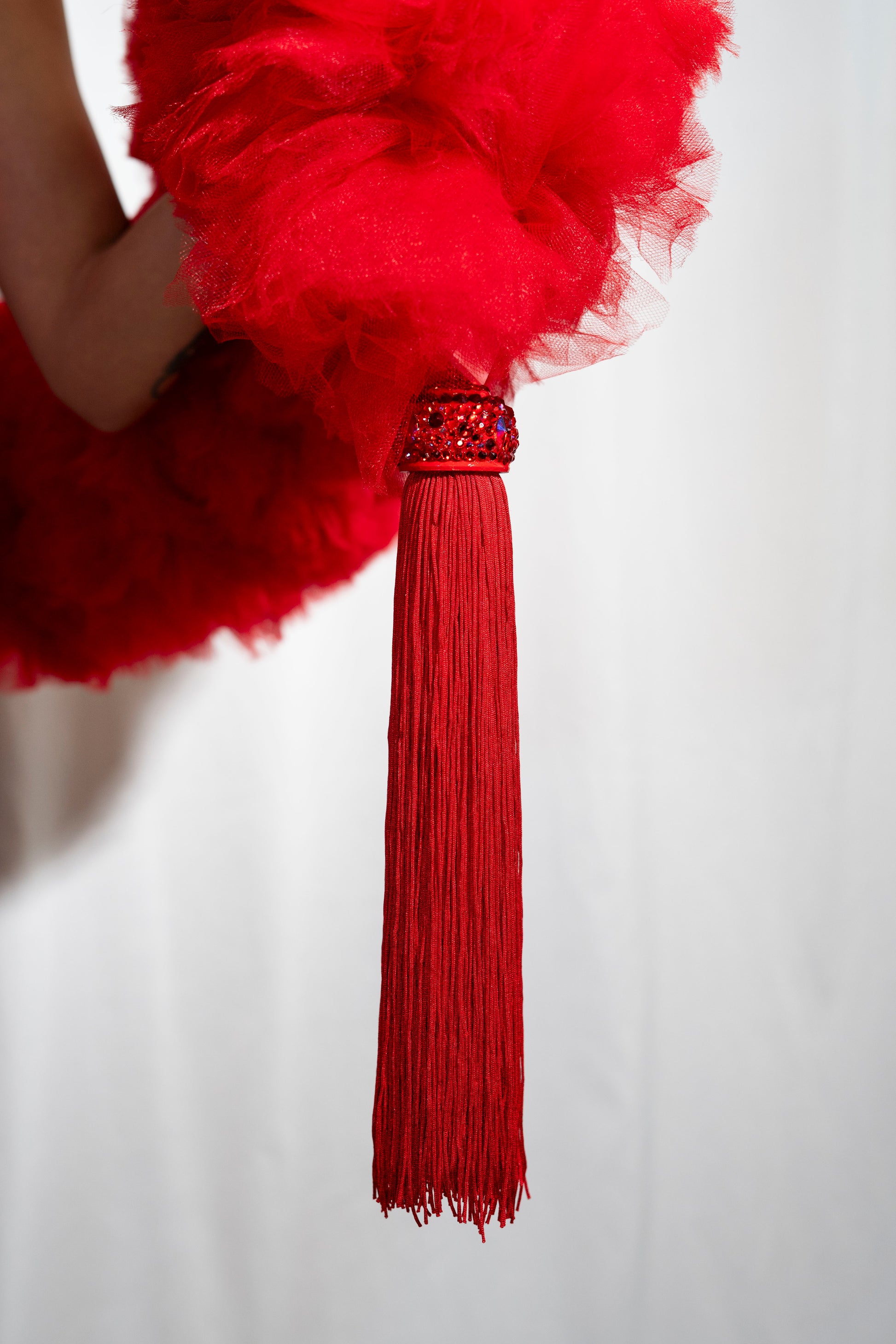 A close-up of The Dazzle - Tulle Boa by Viva La Bombshell Burlesque, featuring a red tasseled accessory with a beaded top against a white background. Each boa is made to order for a unique, elegant touch.