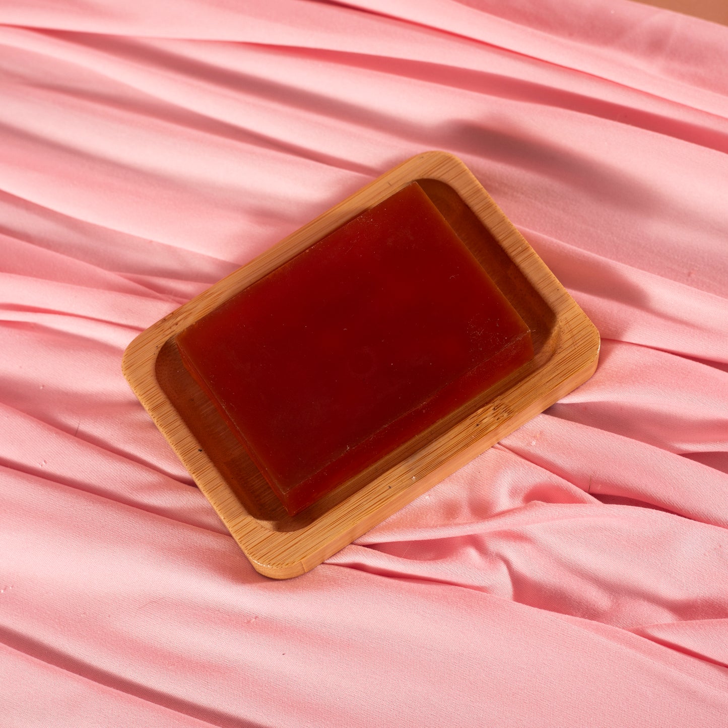 A rectangular Viva La Bombshell Burlesque Turmeric Soap bar sits on a wooden dish atop soft pink fabric—ideal for even skin tone and hydration.