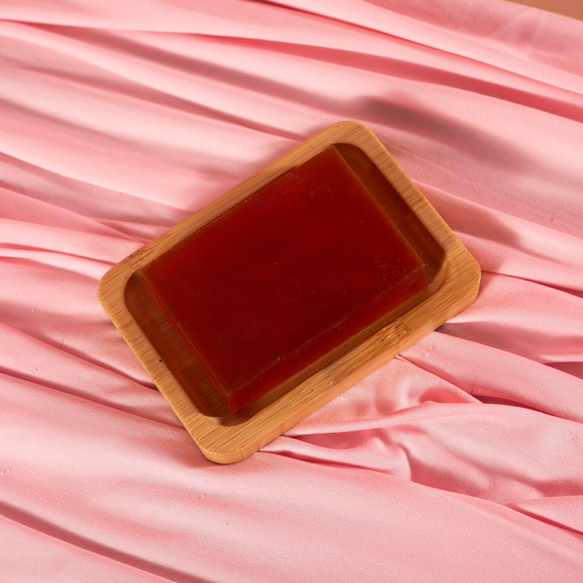 A rectangular Viva La Bombshell Burlesque Turmeric Soap bar sits on a wooden dish atop soft pink fabric—ideal for even skin tone and hydration.