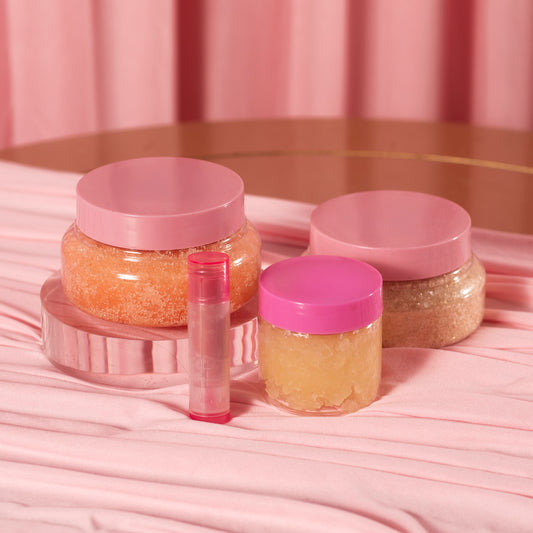 The Diamond Set by Viva La Bombshell Burlesque features three colorful body scrubs and a translucent lip balm tube, artfully arranged on draped pink fabric with a matching pink backdrop.