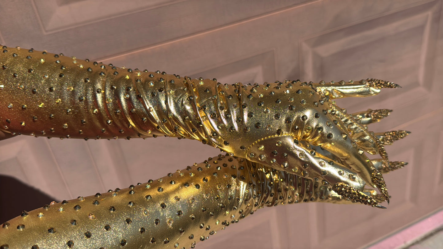 Metallic gold nail gloves with gold rhinestones against a textured background. 