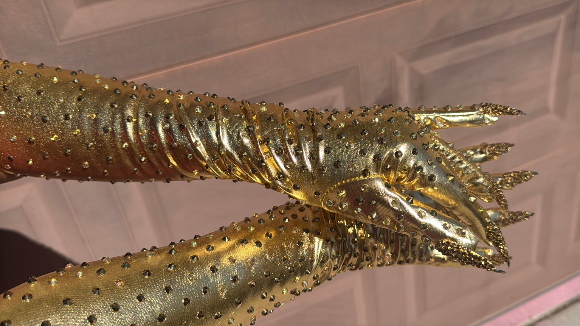 Metallic gold nail gloves with gold rhinestones against a textured background. 