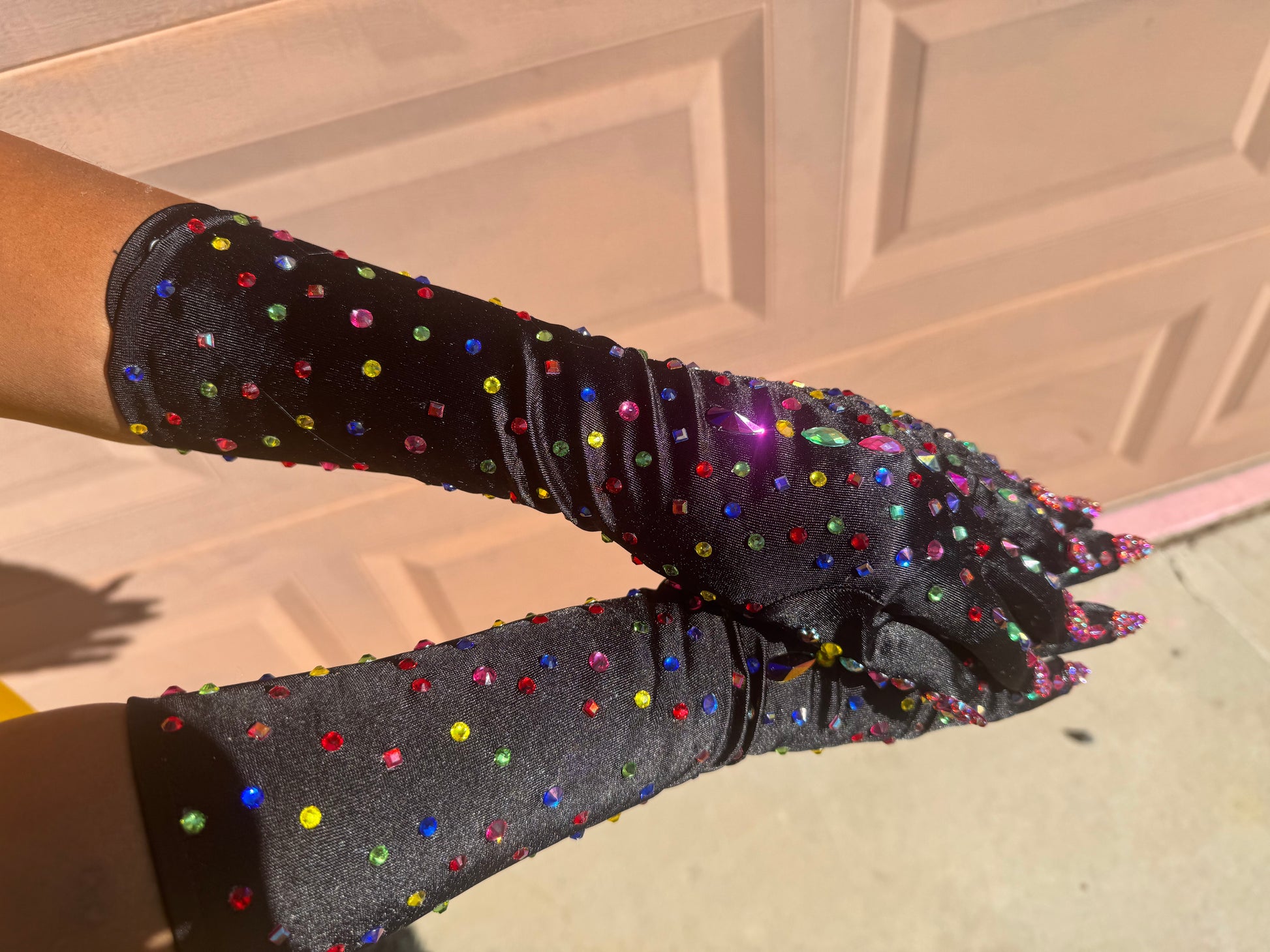 Black nail gloves with multiple rhinestones colors against a textured background. 