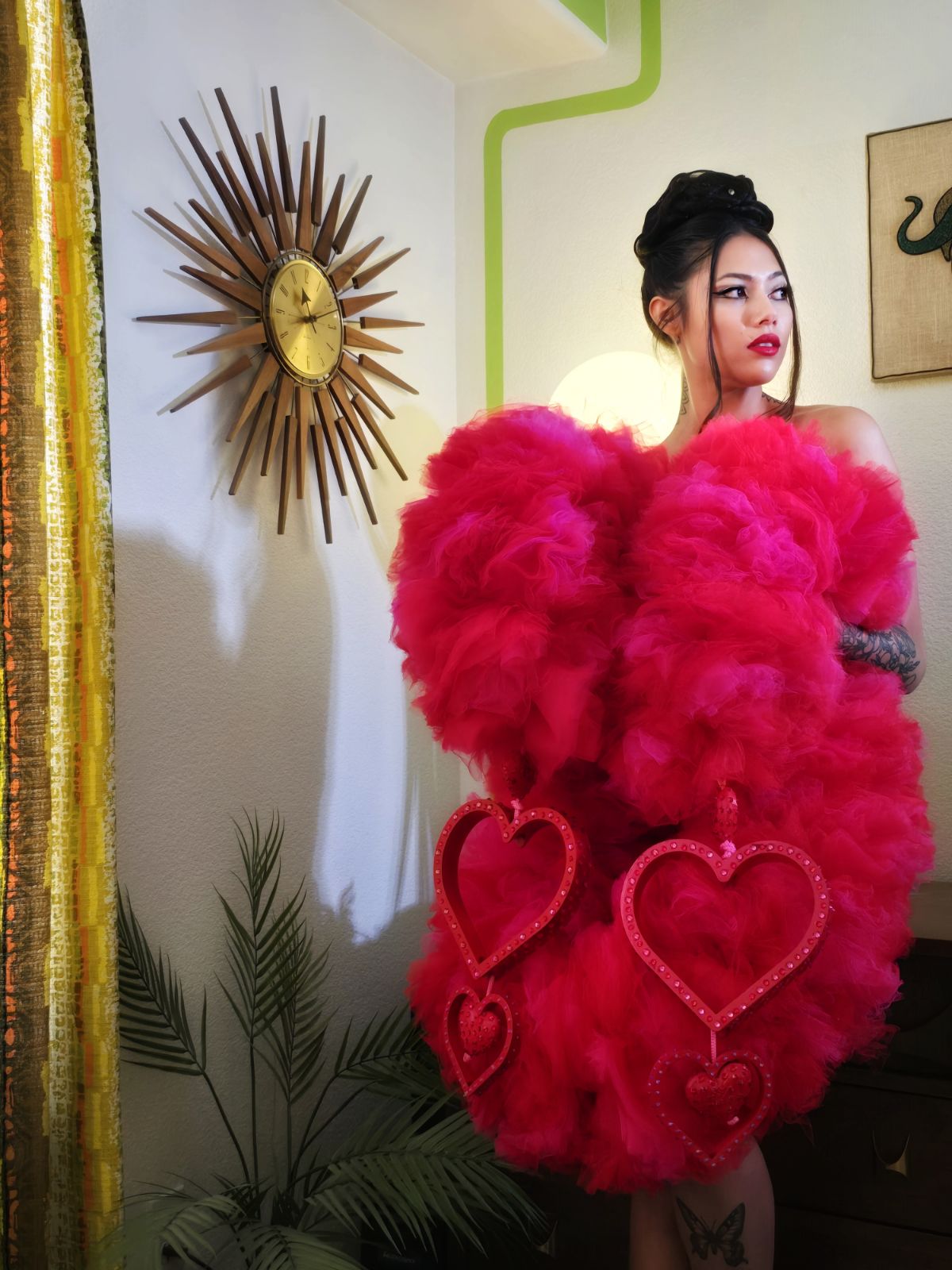 Girl in a decorative room holding a pink and red tulle boa with heart bangles in front of her. 