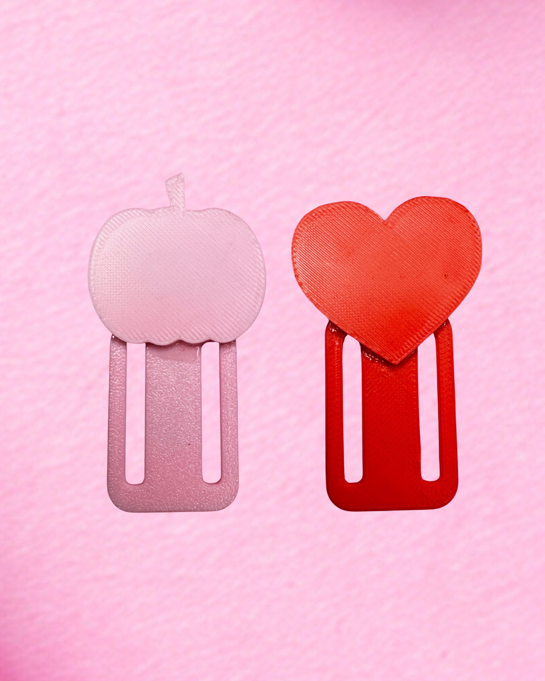 Two large paper clips from Viva La Bombshell Burlesque are shown vertically on a pink background. The left is light pink with an apple top, and the right is a TipSlider in red, featuring a heart-shaped top.