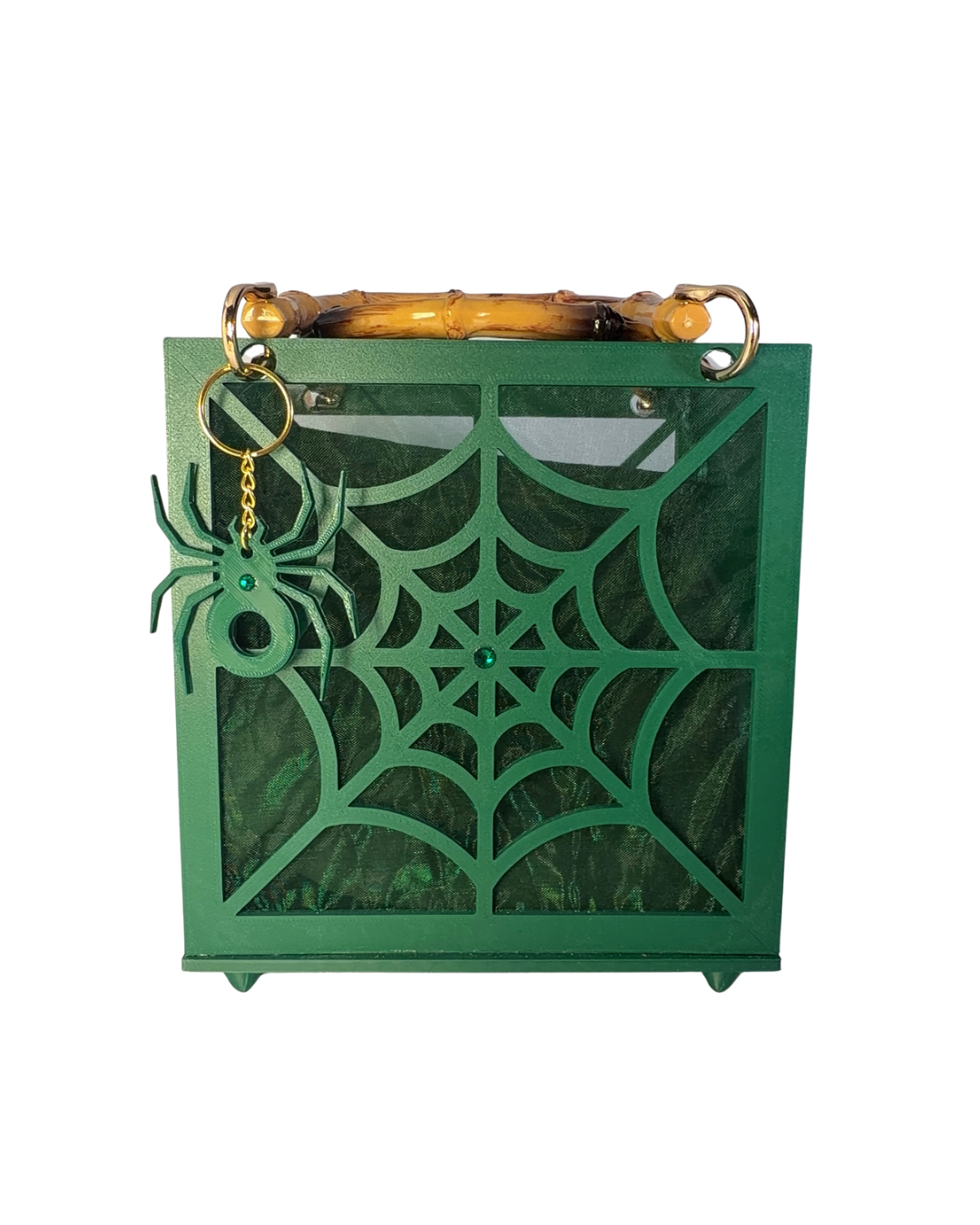 Introducing The Widow – Spiderweb Purse by Viva La Bombshell Burlesque: a green square handbag adorned with a striking spiderweb motif on the front, finished with elegant bamboo handles and accented by a spider-shaped keychain hanging from one side.
