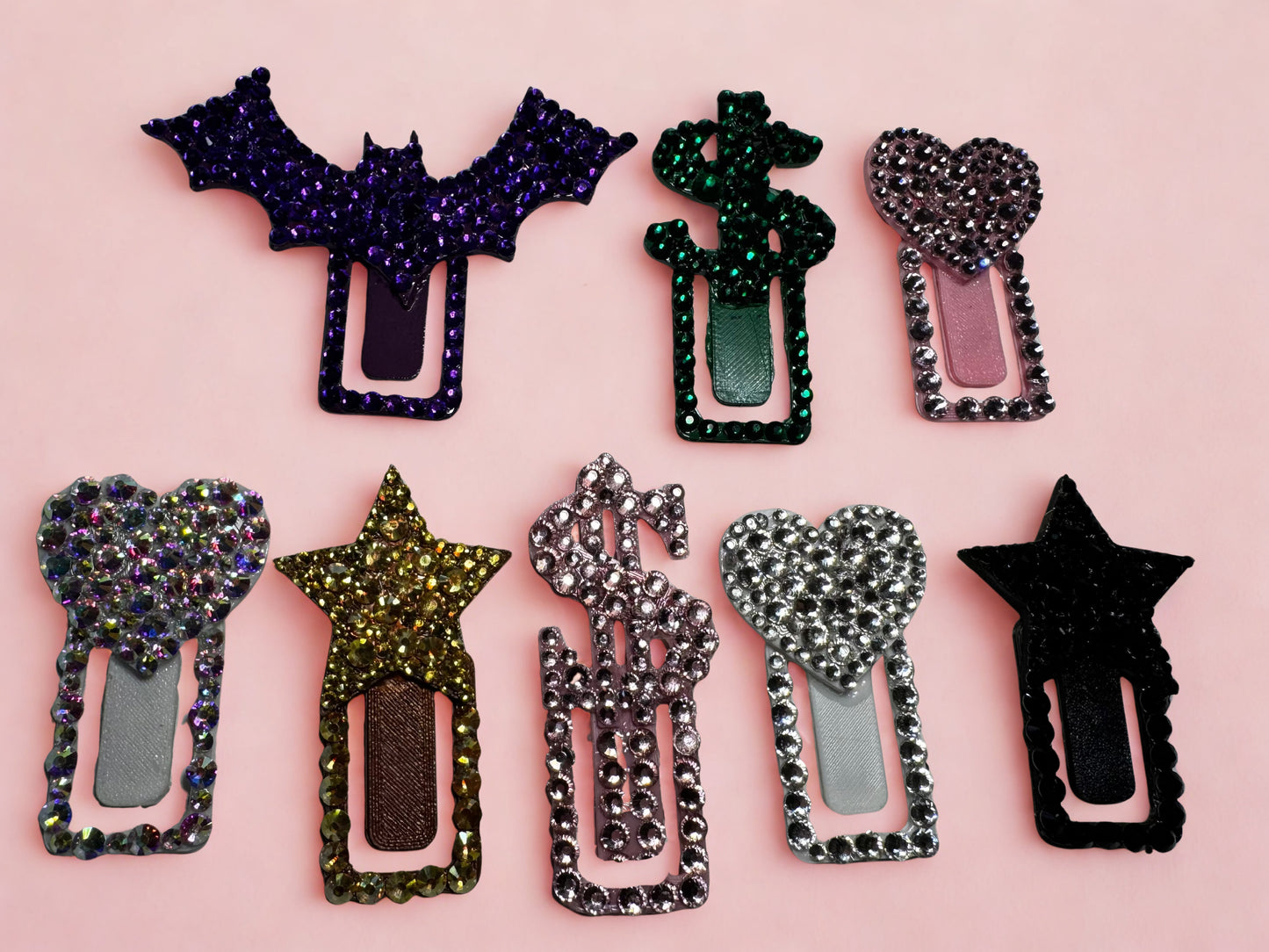 Eight Viva La Bombshell Burlesque TipClips—sparkly paper clips with heart, star, dollar sign, and bat tops—are shown on light pink. Each 3D-printed clip features colorful rhinestones for a fun workspace accessory.