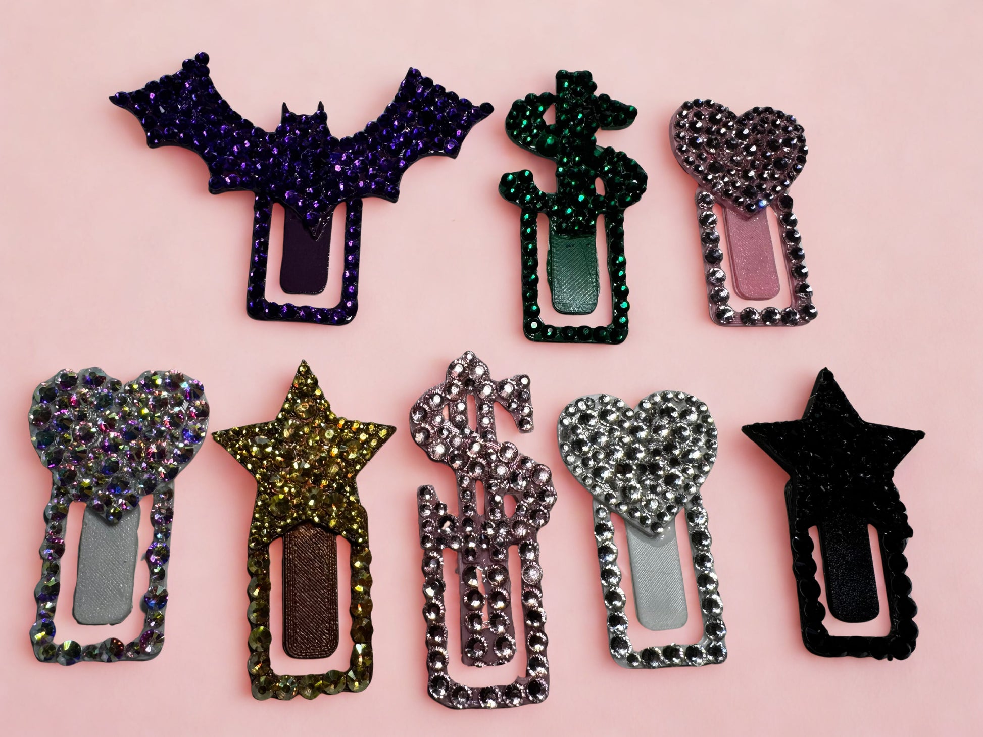 Eight Viva La Bombshell Burlesque TipClips—sparkly paper clips with heart, star, dollar sign, and bat tops—are shown on light pink. Each 3D-printed clip features colorful rhinestones for a fun workspace accessory.