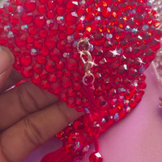 A hand holding a red  rhinestoned pasties with red tassels. Pink rhinestoned pasties with pink tassels, shown next to it on a countertop.