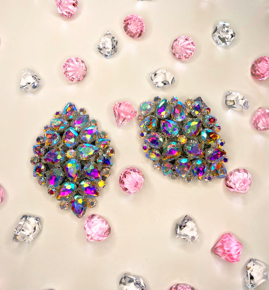 Two ornate Big Spender Pasties by Viva La Bombshell Burlesque, adorned with iridescent jewels, are displayed on a light beige surface amid scattered pink and clear faceted acrylic gems.