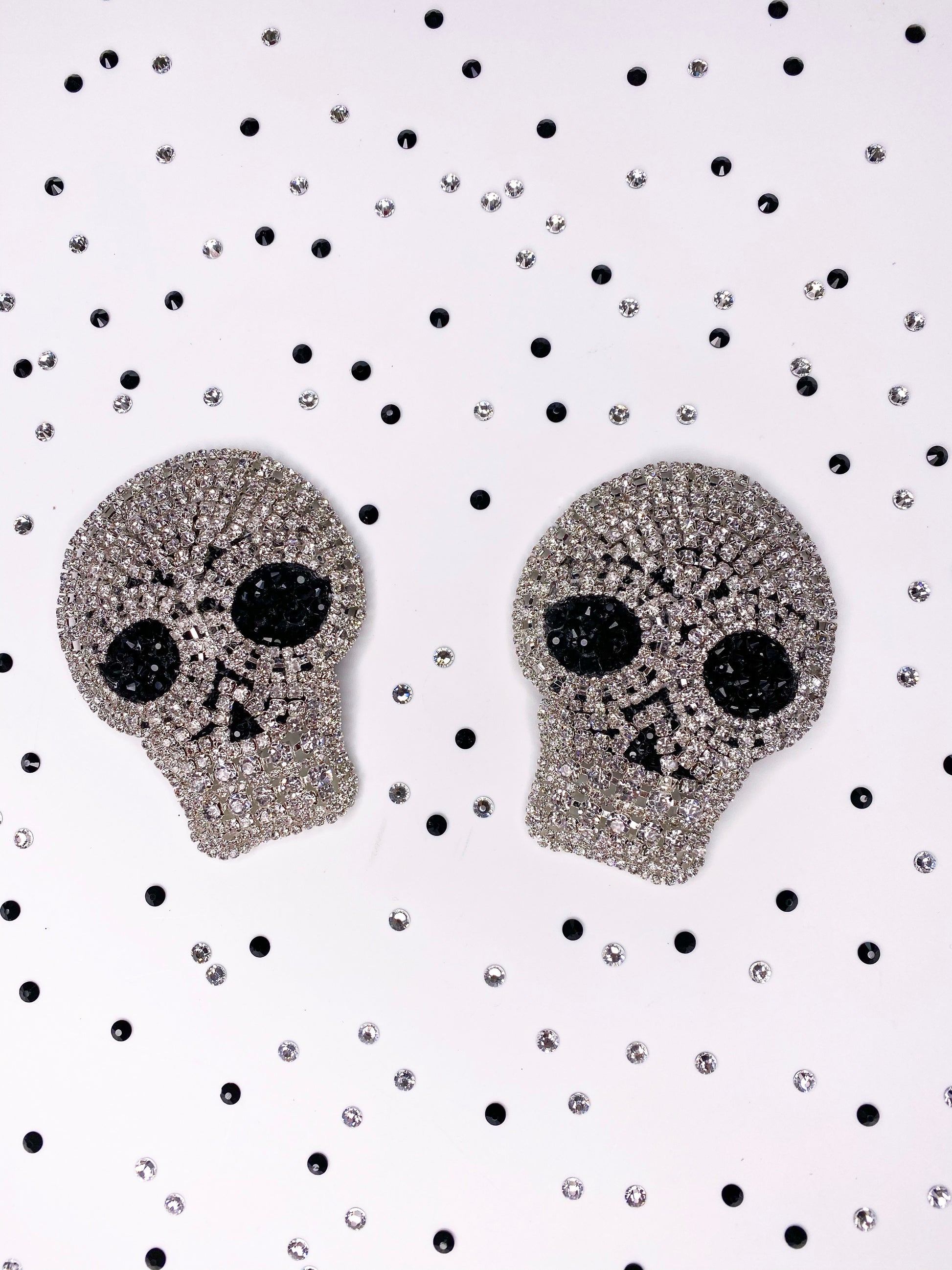 A straight on photo of a pair of clear rhinestone skull applique with black rhinestone eyes pasties 