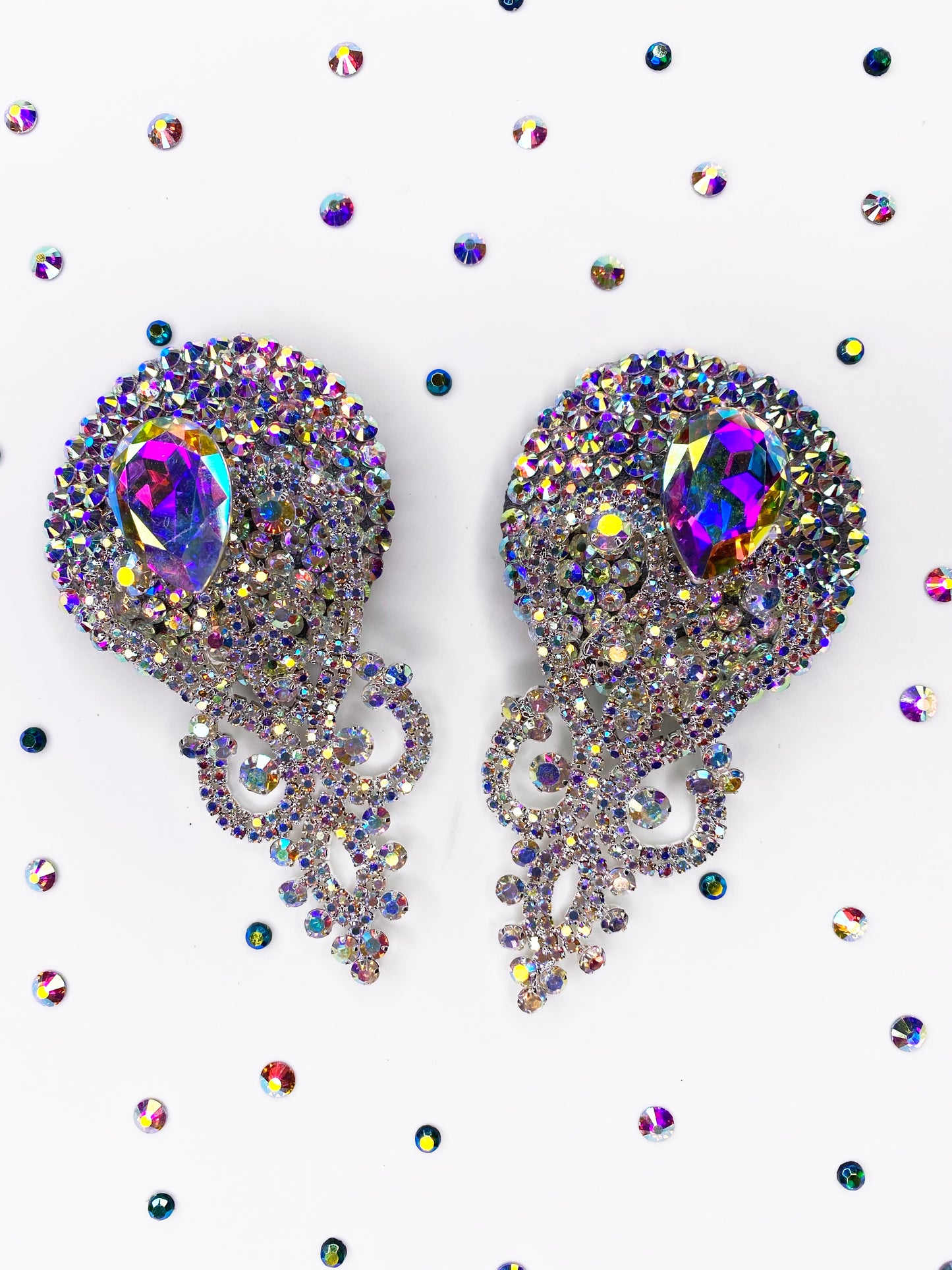Showgirl Pasties by Viva La Bombshell Burlesque feature ornate, jeweled designs with iridescent stones and swirling patterns, evoking vintage glamour. Displayed on white, they're surrounded by small, colorful crystal rhinestones.