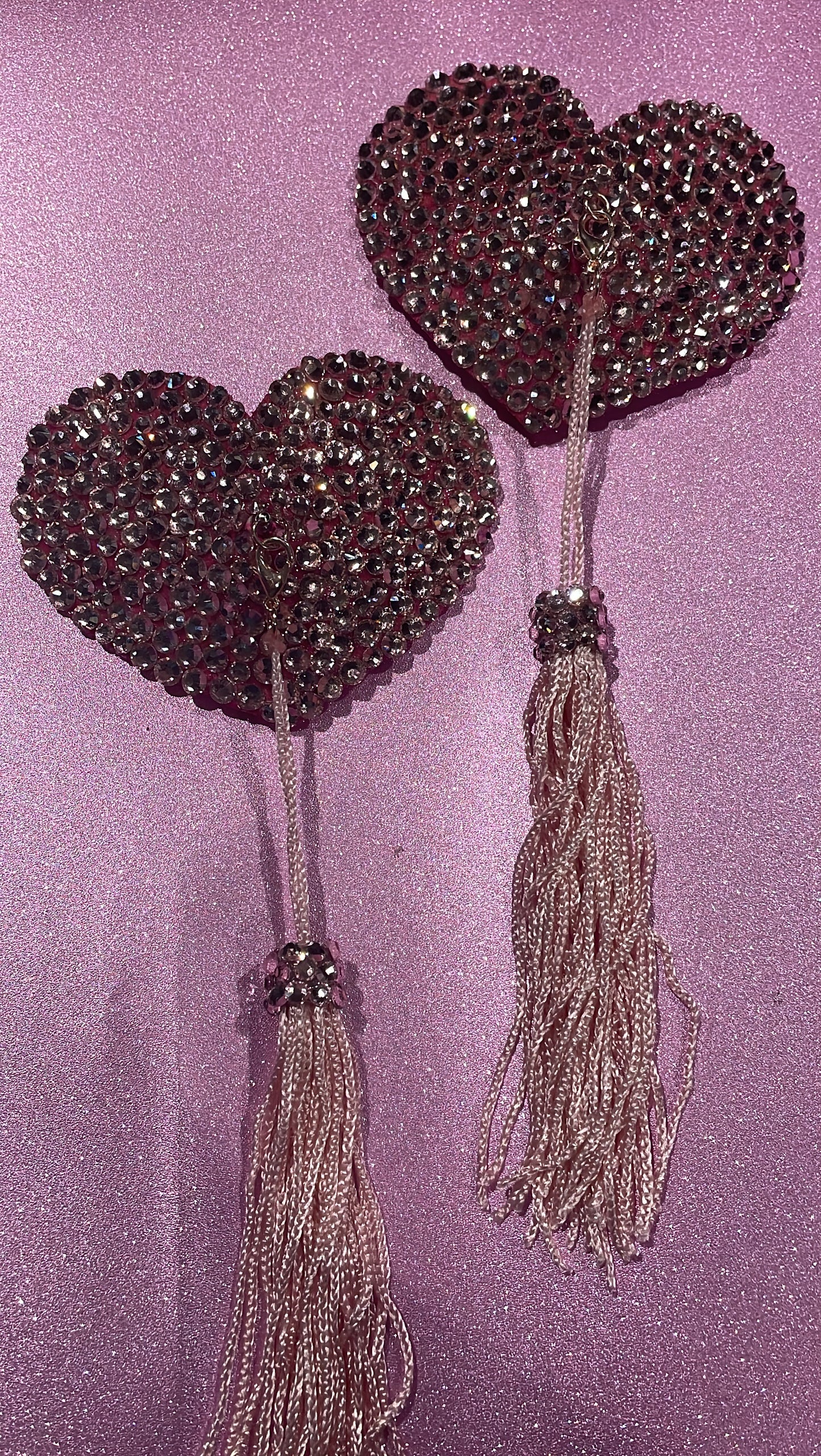 Pink rhinestoned heart shaped pasties with pink tassels on a glitter pink background. 