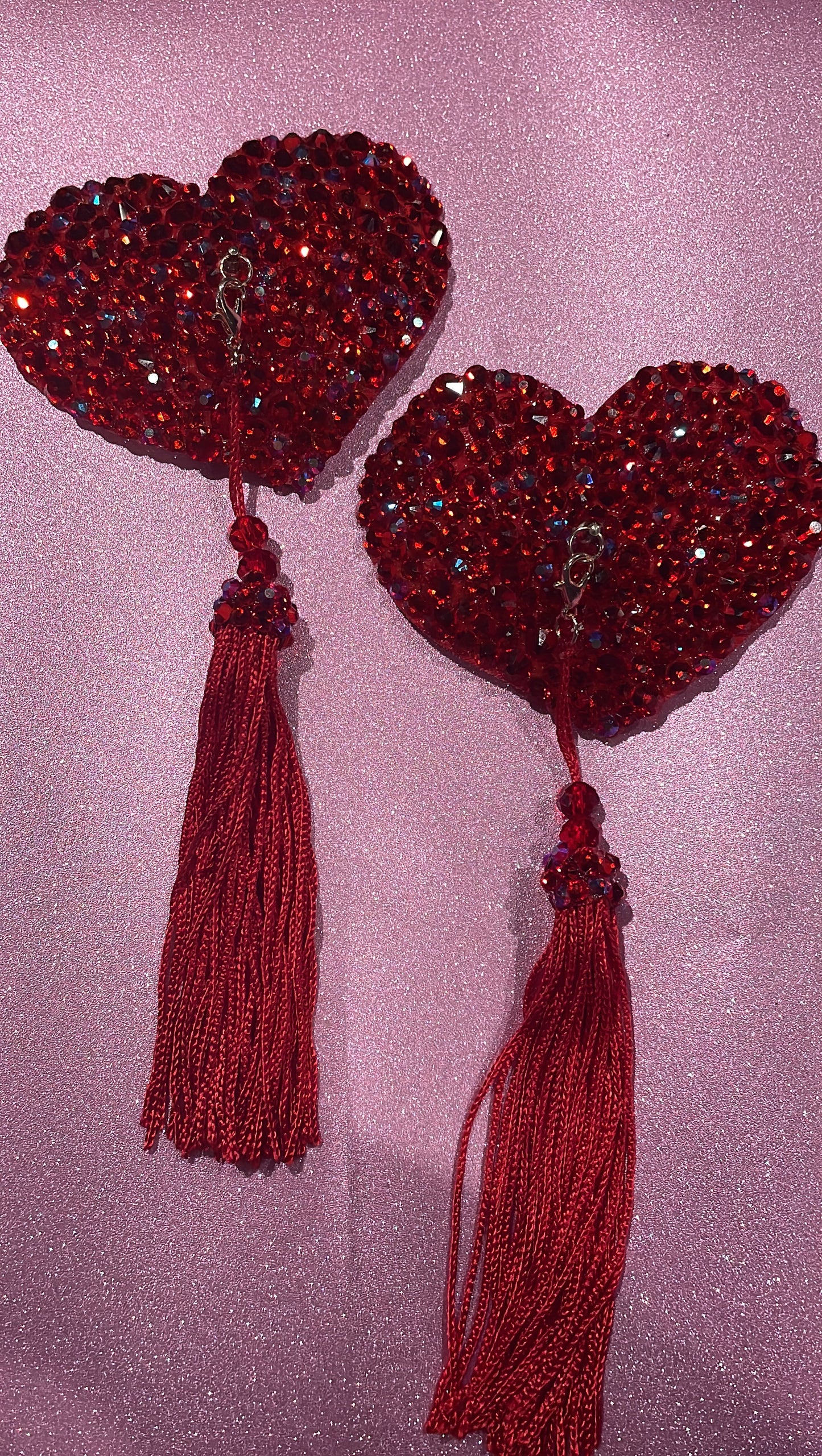 Red rhinestoned heart shaped pasties with red tassels on a glitter pink background. 