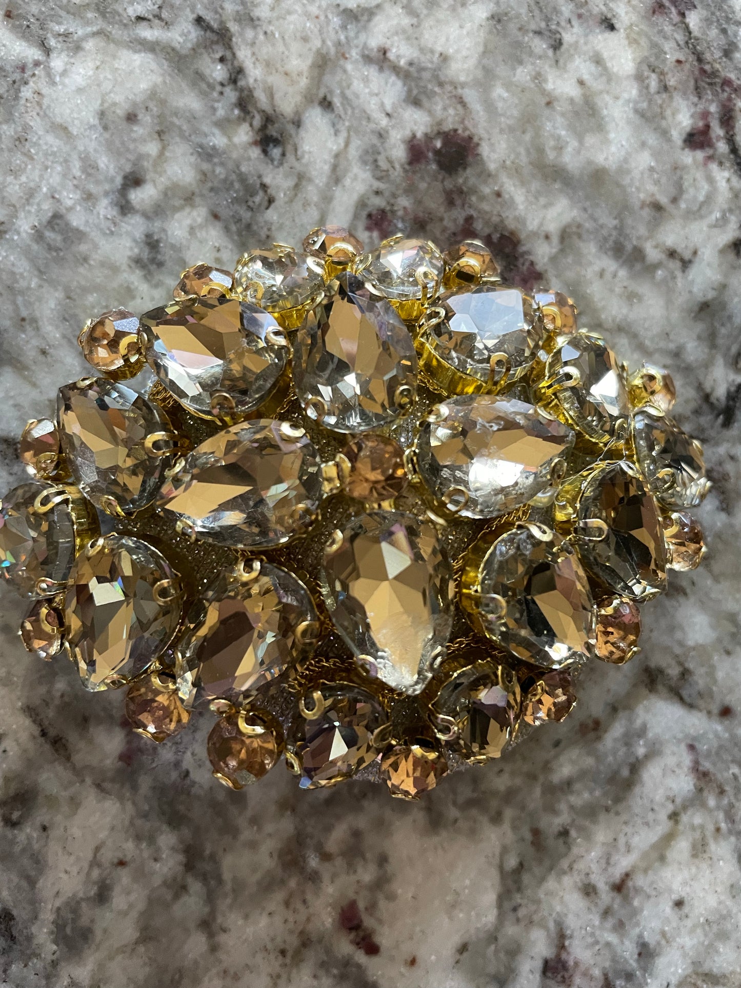 A close-up of Viva La Bombshell Burlesque's Gold Digger Pasties, shimmering with faceted teardrop and round crystals, displayed against a textured stone background.