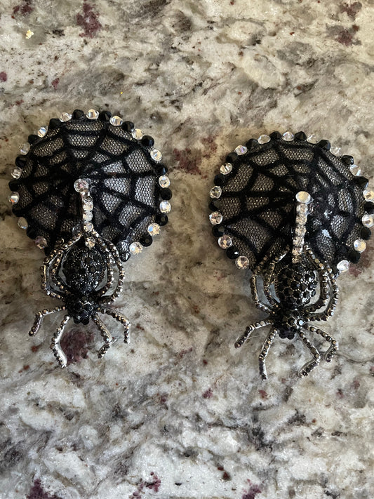 Viva La Bombshell Burlesque's Mistress of the Dark Pasties feature black spider figures on sparkling rhinestone webs, evoking Elvira style—perfect for a dramatic burlesque look. Shown on a light mottled surface.