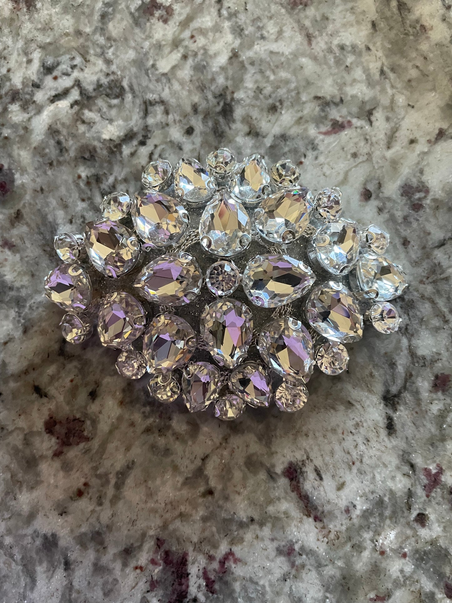 The Million Dollar Baby Pasties by Viva La Bombshell Burlesque feature sparkling, oval designs with clear faceted crystals in a symmetrical pattern, displayed on a textured, light-toned stone surface.
